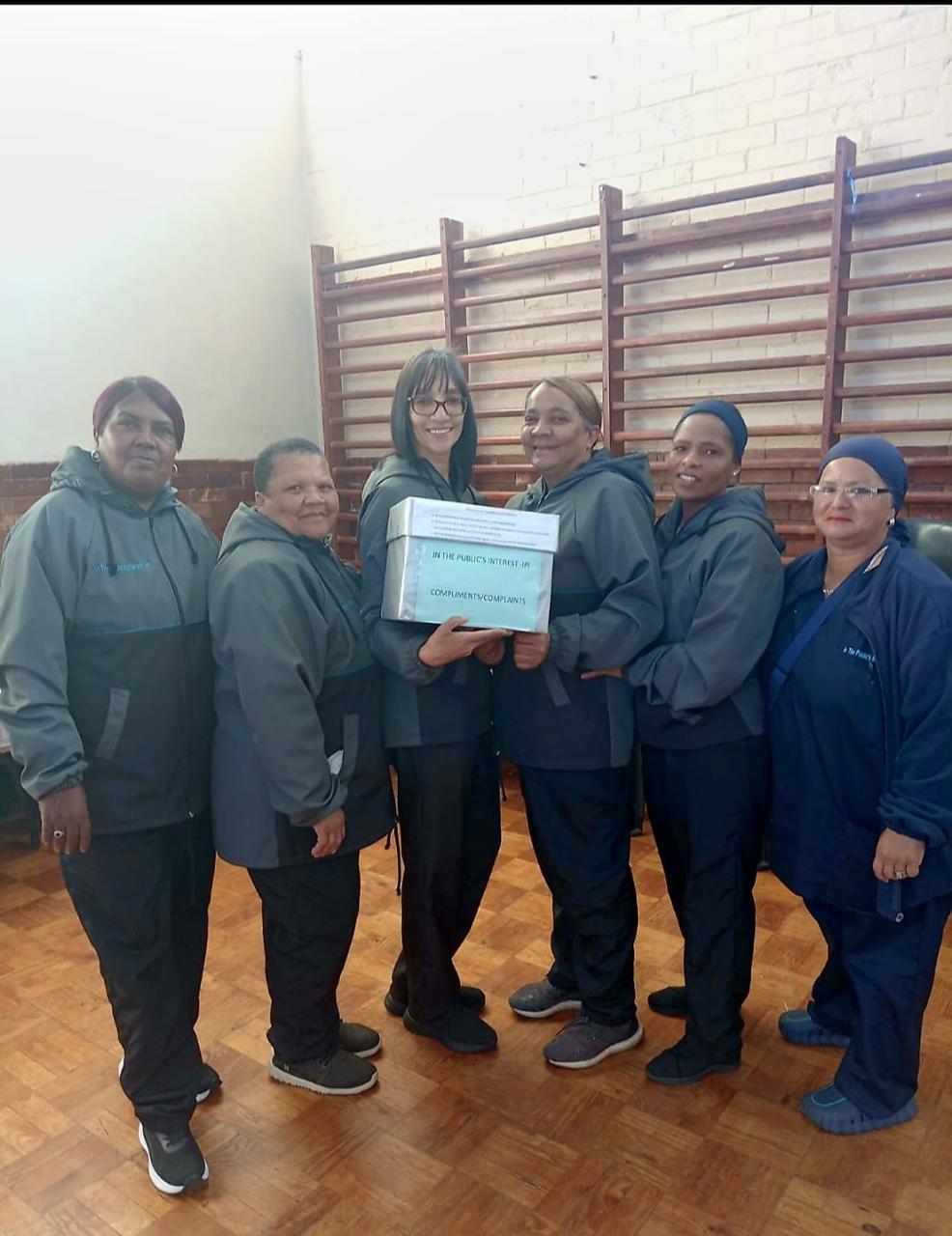 IPI care workers holding the In the Public's Interest compliments and complaints box at a community hall in Cape Town